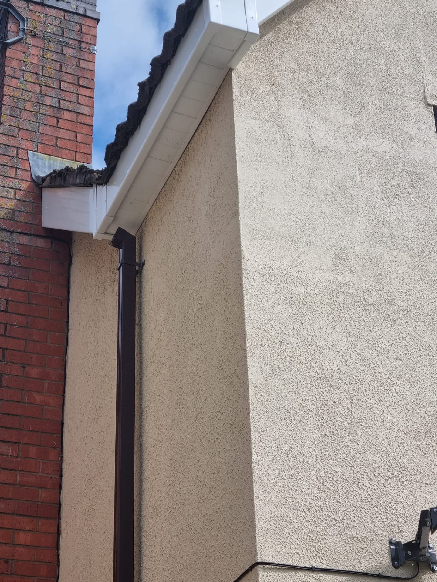 Replacement white fascia and soffit detail on a rendered gable beside a brick chimney