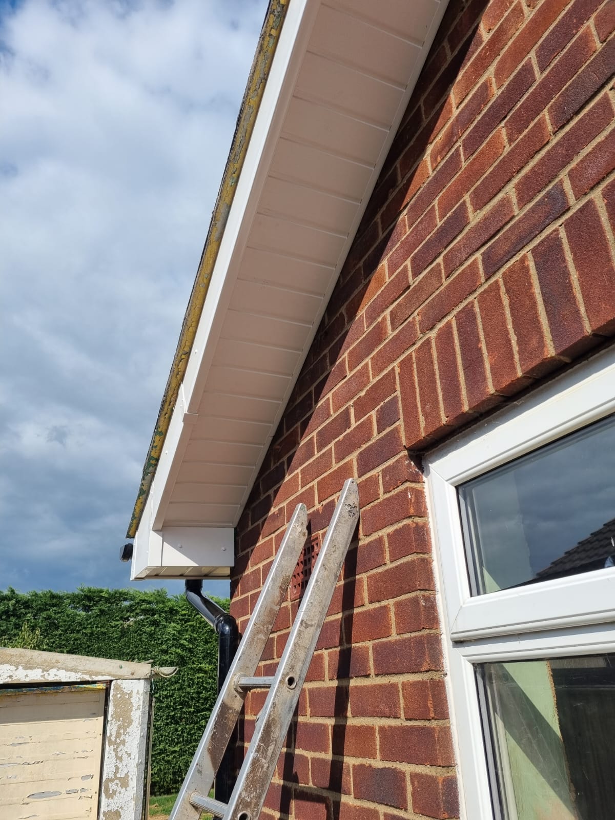 New white fascia and soffit board fitted to a brick gable end with black downpipe